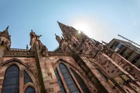 Freiburger Münster von unten, gotischer Sandsteinturm mit Fialen und Maßwerk gegen blauen Himmel