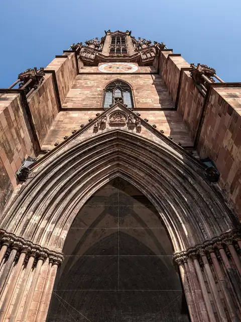 Freiburger Münster, Blick von unten auf den gotischen Turm mit Uhr und Sandsteinfassade