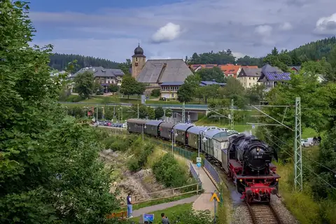 Historischer Dampfzug der Dreiseenbahn fährt durch Schluchsee, im Hintergrund Kirche und Ortskern