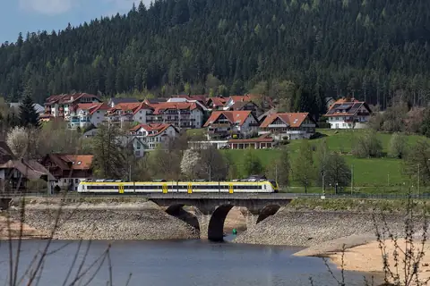 Zug der Dreiseenbahn überquert Steinbrücke am Titisee vor Ortspanorama und Wald
