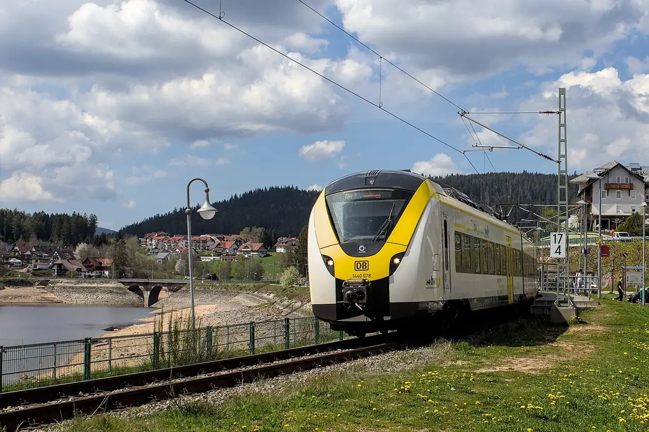 Regionalzug der Dreiseenbahn (BR 1440) an einem Bahnsteig vor Schwarzwald-Panorama und Stausee