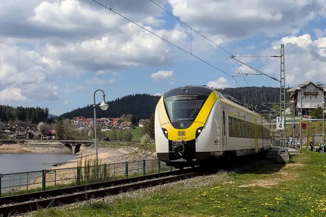Regionalzug der Dreiseenbahn (BR 1440) an einem Bahnsteig vor Schwarzwald-Panorama und Stausee