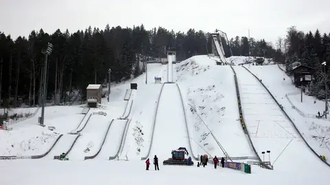 Skisprungschanzen-Anlage im Schnee mit Besuchern am Auslauf, Wald im Hintergrund