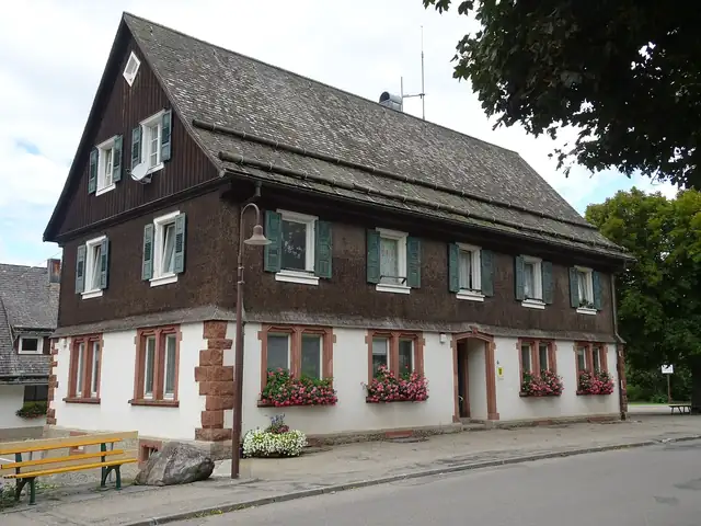 Traditionelles Schwarzwaldhaus mit dunkler Holzverschindelung, grünen Fensterläden und Blumenkästen
