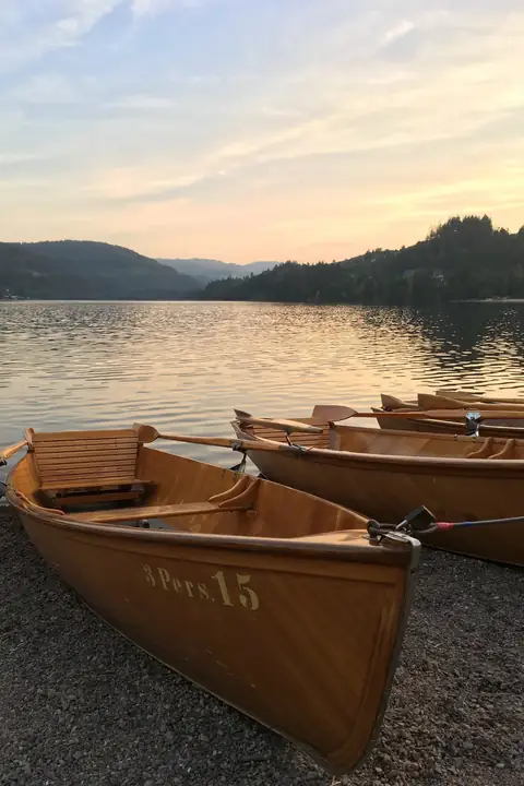 Holzruderboote am Ufer des Titisees bei Sonnenuntergang, im Hintergrund bewaldete Hügel