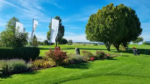 Clubgelände des Golfclubs Obere Alp mit drei Fahnen, Staudenbeeten und einem Golftrolley am Rand des Grüns