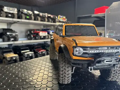 Orangefarbenes ferngesteuertes Geländemodell eines Ford Bronco, dahinter Regale mit weiteren Modellautos