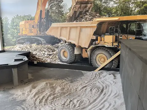 Sandbereich in der Halle vor einer großen Wandgrafik mit Bagger und Muldenkipper