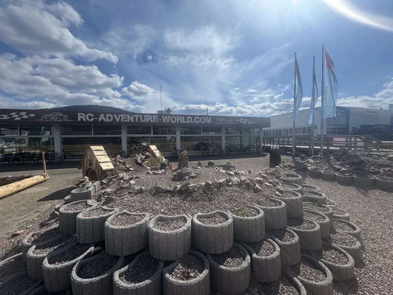 Außengelände der RC Adventure World mit Crawler-Parcours aus Pflanzsteinen, dahinter die Halle mit dem Schriftzug RC-Adventure-World.com