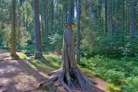 Geschnitzte Zauberer-Holzfigur an einem Baumstumpf am Zauberwald-Pfad im Waldgebiet Taubenmoos bei Bernau