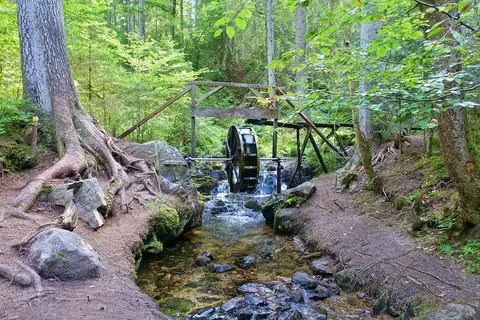 Hölzernes Wasserrad an einem Bachlauf im Wald entlang des Zauberwald-Pfads Bernau