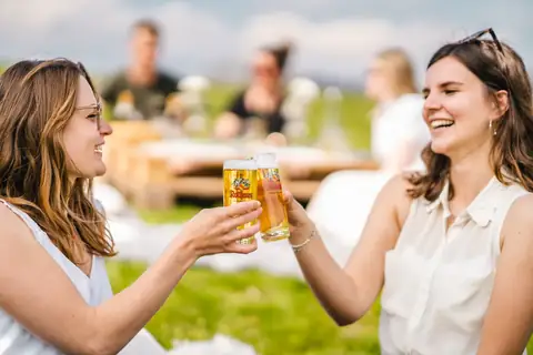 Zwei Frauen stoßen beim Picknick am See mit Rothaus Bier an