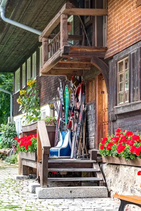 Alte Ski und Stöcke lehnen an einem Schwarzwälder Bauernhaus mit roten Geranien