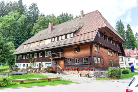 Traditionelles Schwarzwaldhaus mit dunkler Holzschindelfassade, rotem Ziegeldach und Blumenkästen am Eingang