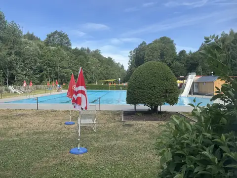 Schwimmerbecken des Freibads Lenzkirch mit Breitrutsche, Kiosk und Sonnenschirmen am Beckenrand