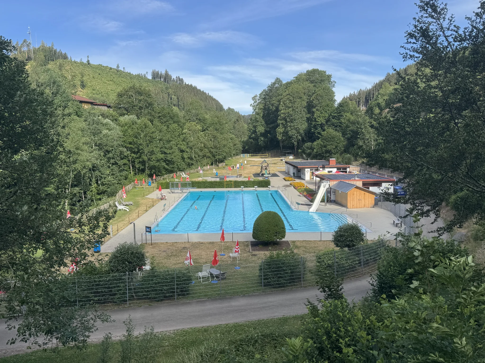 Blick von oben auf das Freibad Lenzkirch mit 50-Meter-Becken, Rutsche und Liegewiese im bewaldeten Haslachtal