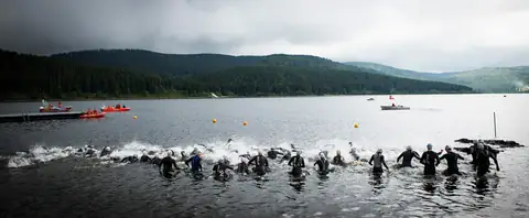 Triathleten beim Schwimmstart im Schluchsee, Schwarzwälder Bergwald im Hintergrund